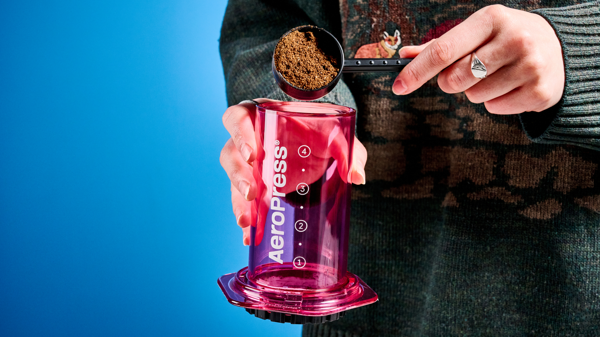 the aeropress clear color in pink photographed against the blue tom's guide background