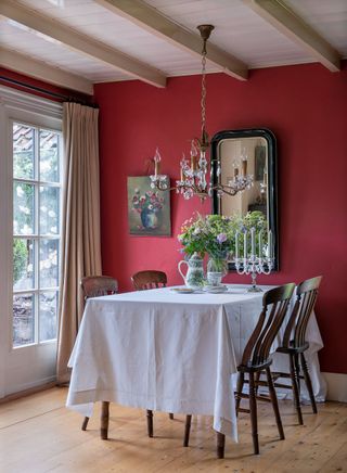 dining table with white cloth in room with red walls chandelier dark wood chairs and french windows