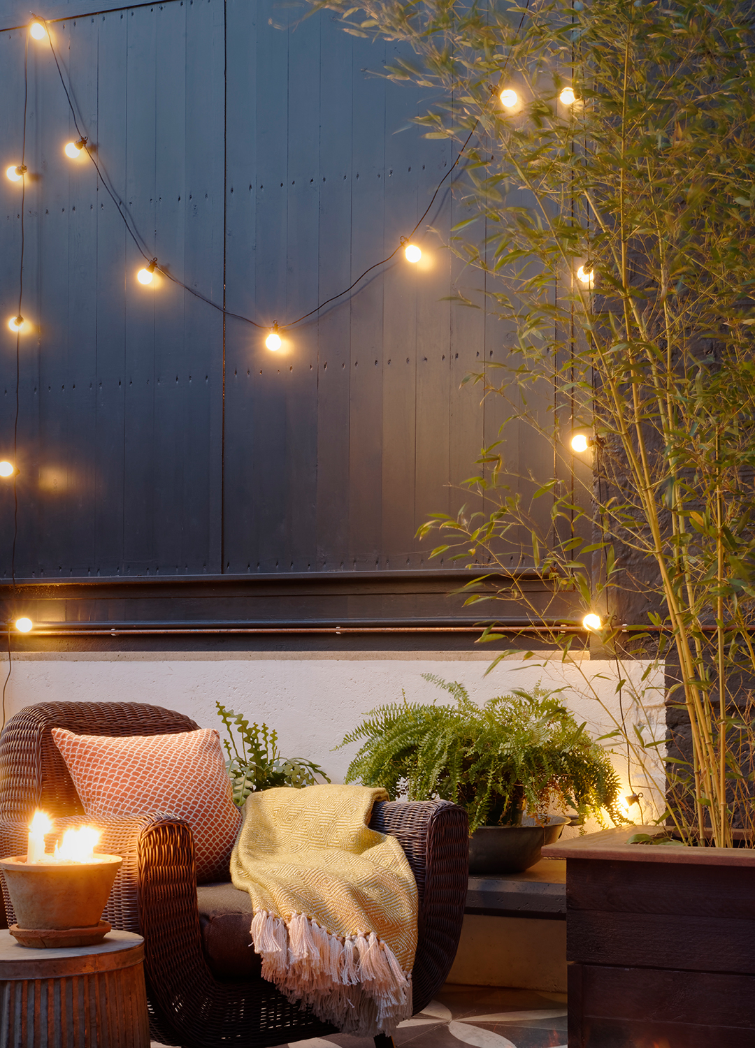 Garden with black painted fences a wicker armchair and festoon lights