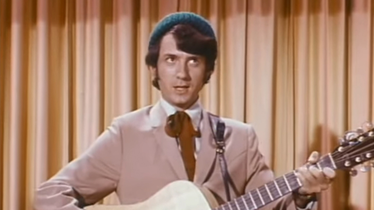 Michael Nesmith in a suit and knit hat, playing guitar on The Monkees