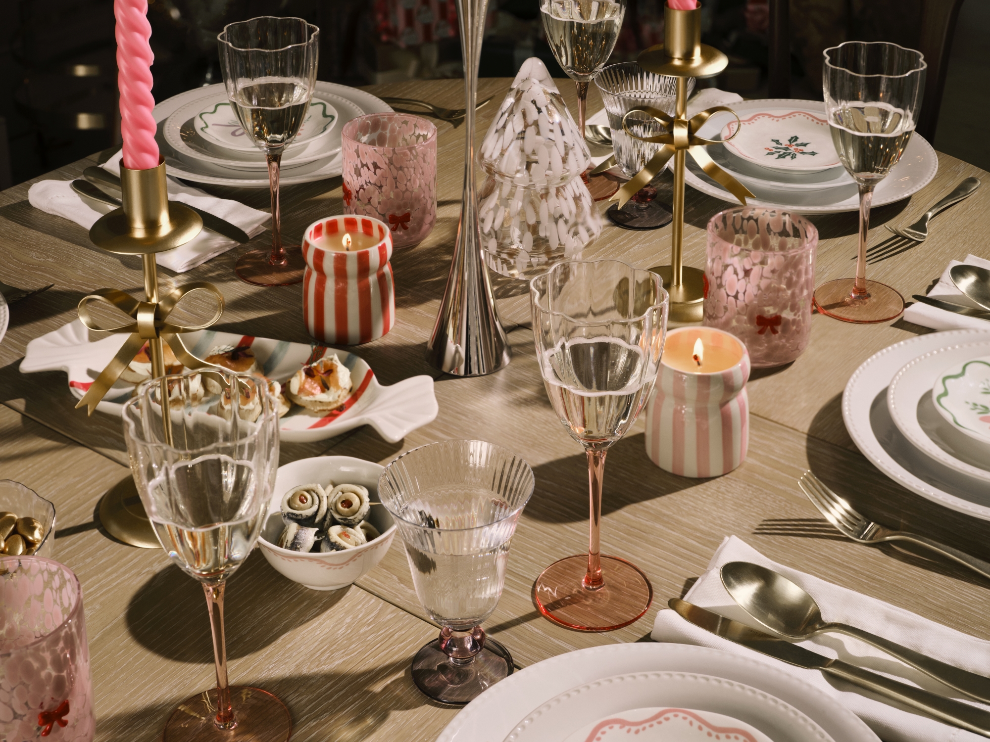 Christmas table setting with gold tablecloth, striped candles, taper candles, and festive dinnerware