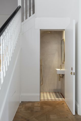 small powder room under stairs with shower, basin and tiled flooring