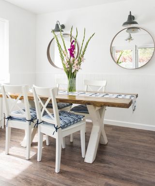 A white room with wood-effect vinyl kitchen floor ideas, white dining table and circular mirrors.