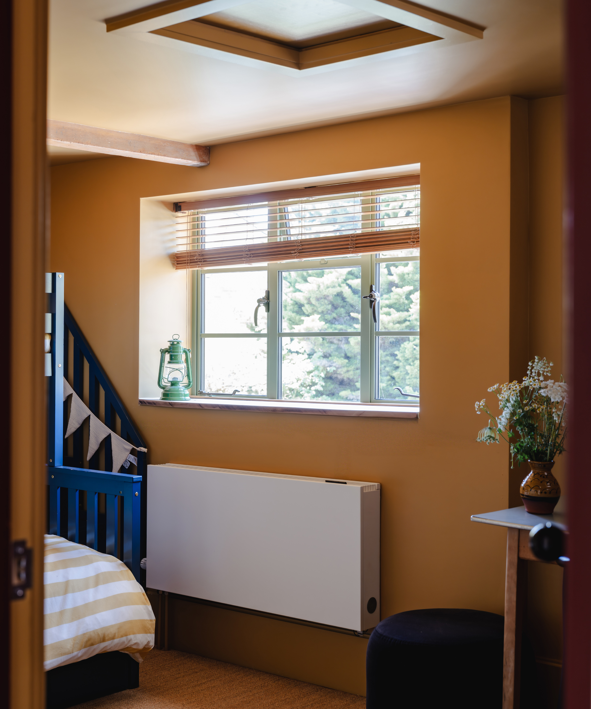 bedroom painted yellow with heat pump compatible radiator below casement window, loft hatch in ceiling above