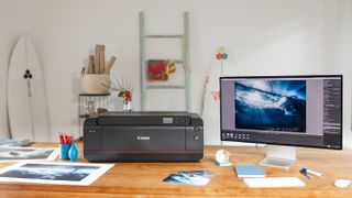 Canon ImagePrograf Pro-1100 on a desk, in a home studio, next to a computer monitor and printed photos