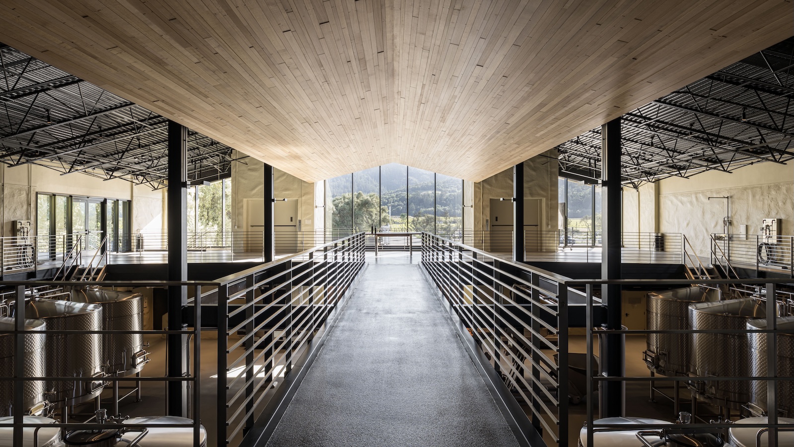 The new Robert Mondavi Winery winemaking facility, with a wooden ceiling and rows of gleaming stainless steel tanks leading to a wall of windows overlooking To Kalon vineyard.