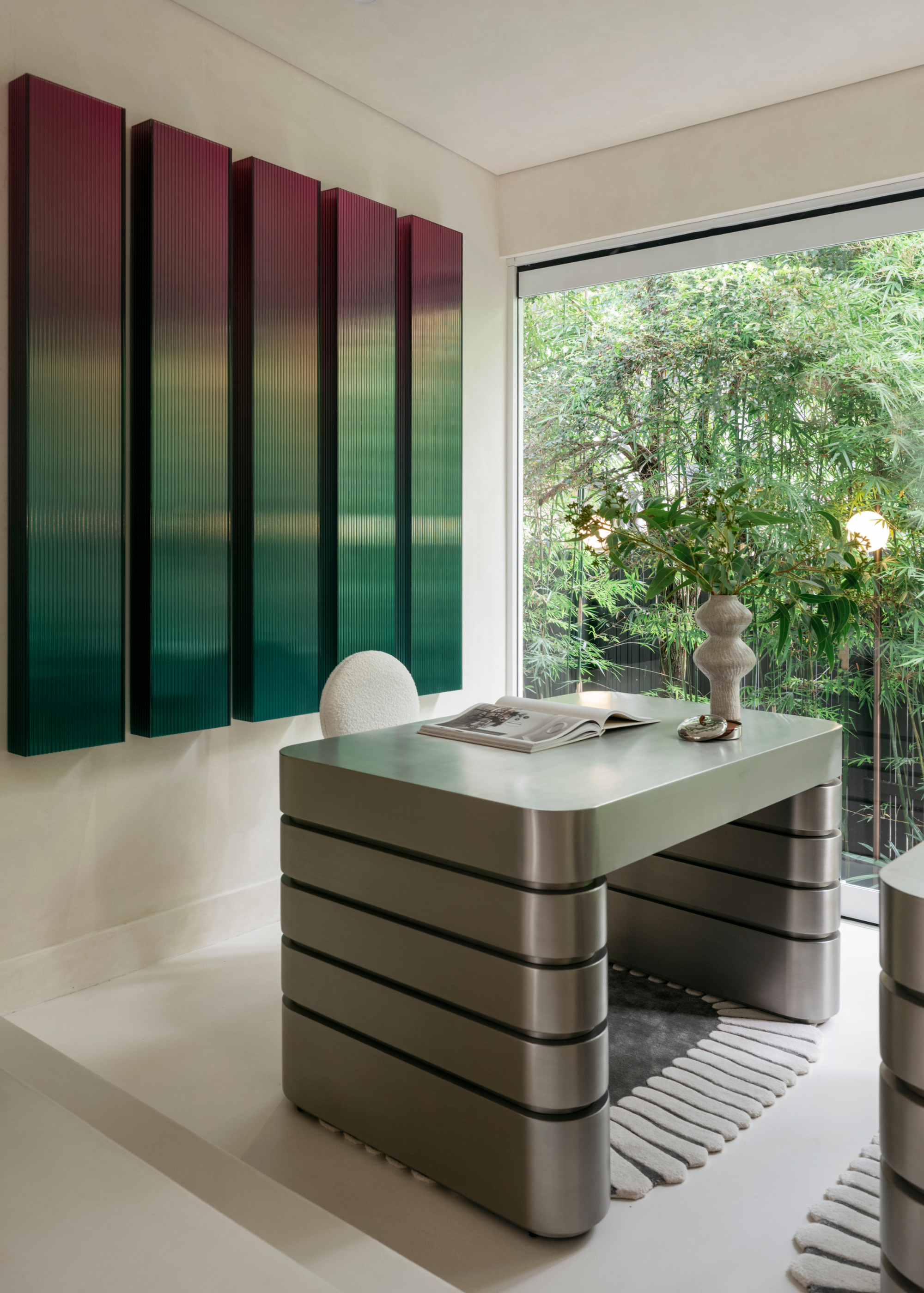 A white office with a large window, a chrome desk with stacked legs, a white chair, and multichrome glass wall features
