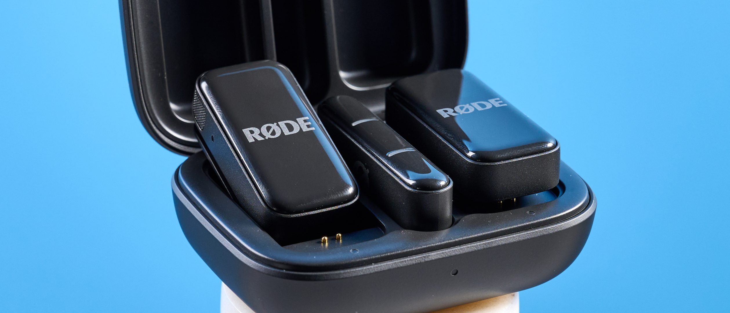 the rode wireless micro microphone with the black charging case and two black transmitter mics photographed against a blue background