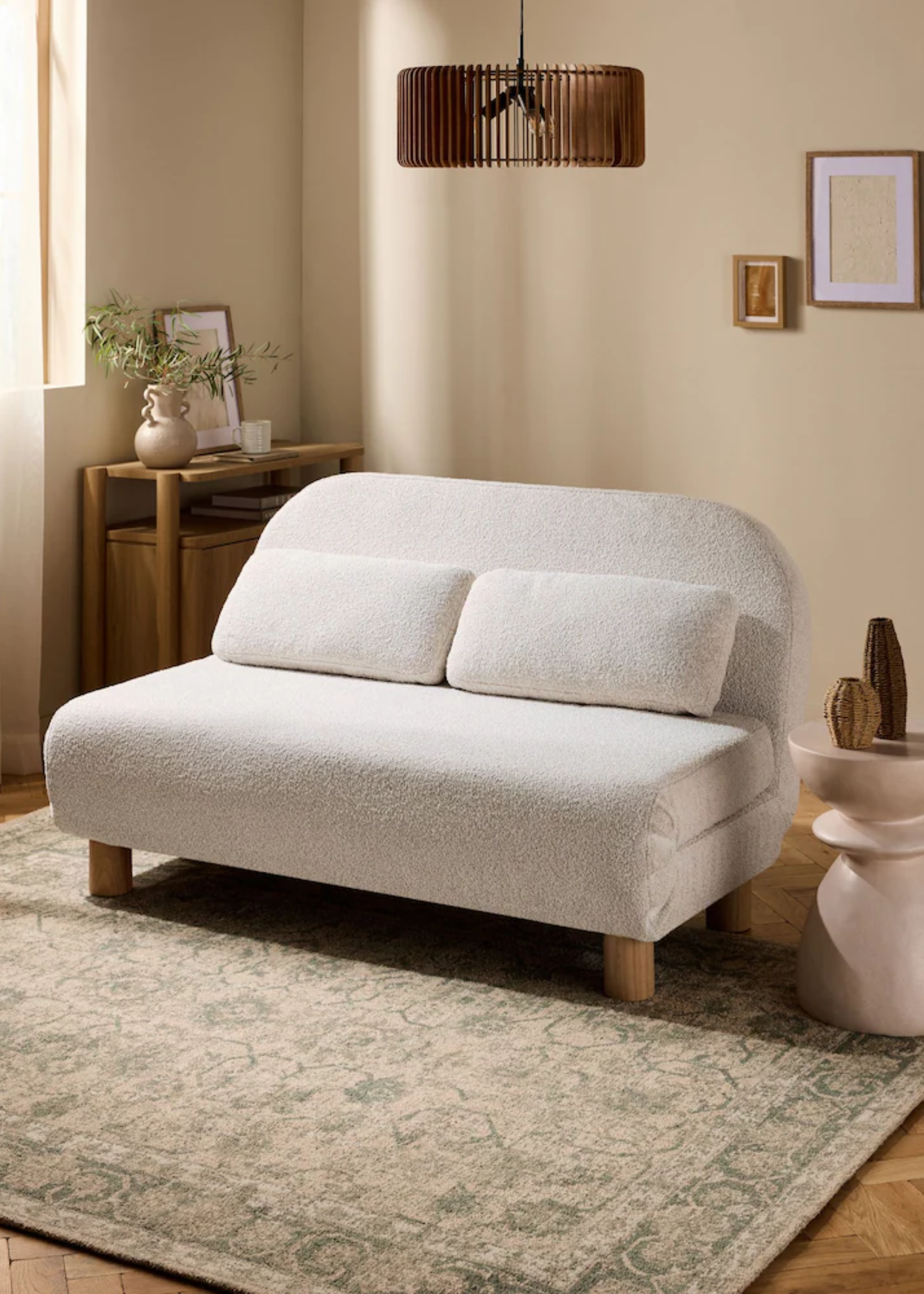 A cream boucle sofa bed on a Persian rug by a side table with woven vases