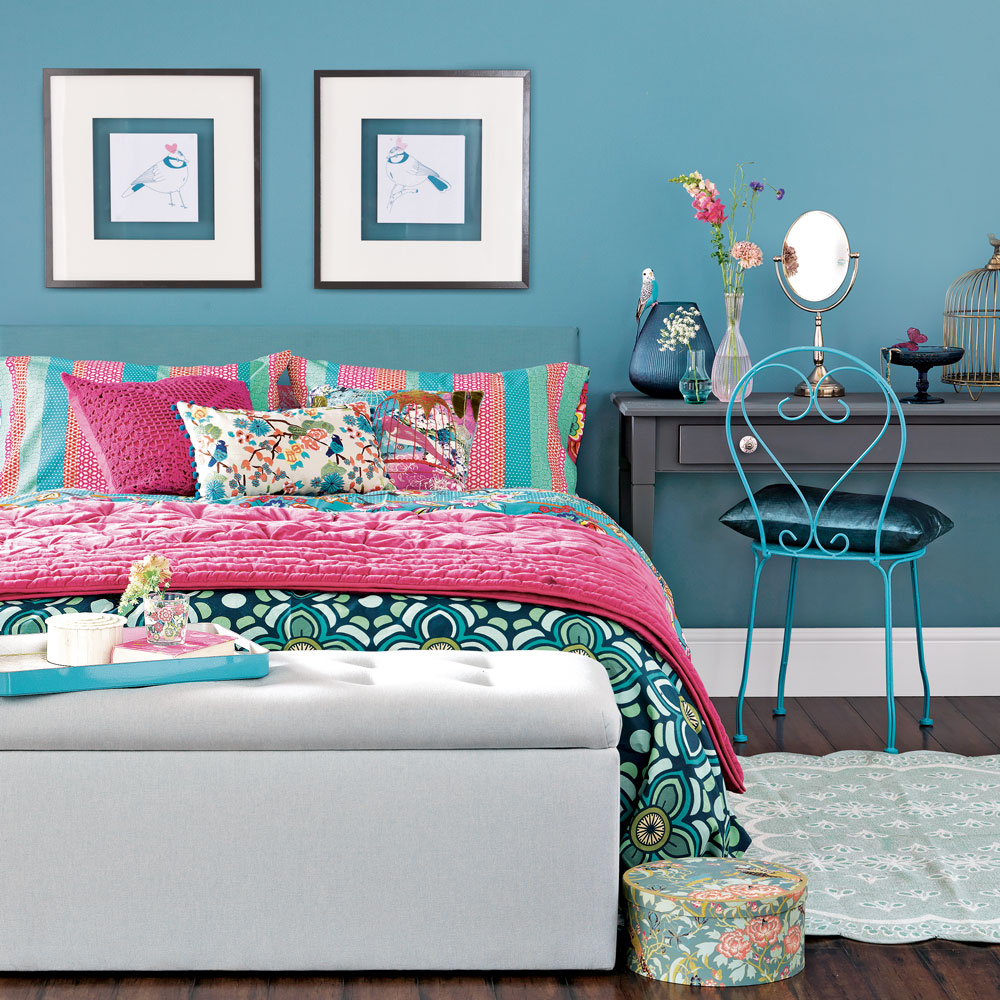 blue bedroom with colourful bedding, storage ottoman and dressing table