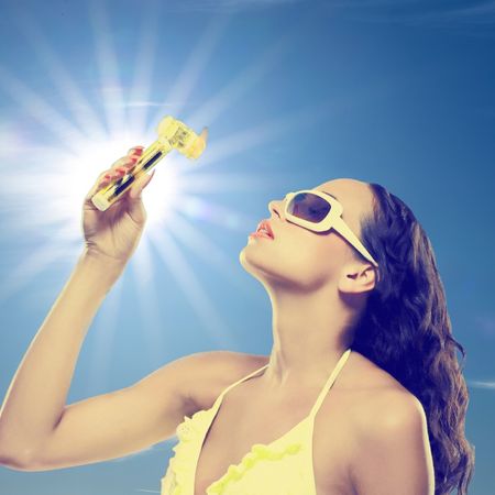 a white woman with dark hair wearing a yellow bikini top holding a yellow fan against the sun and sky