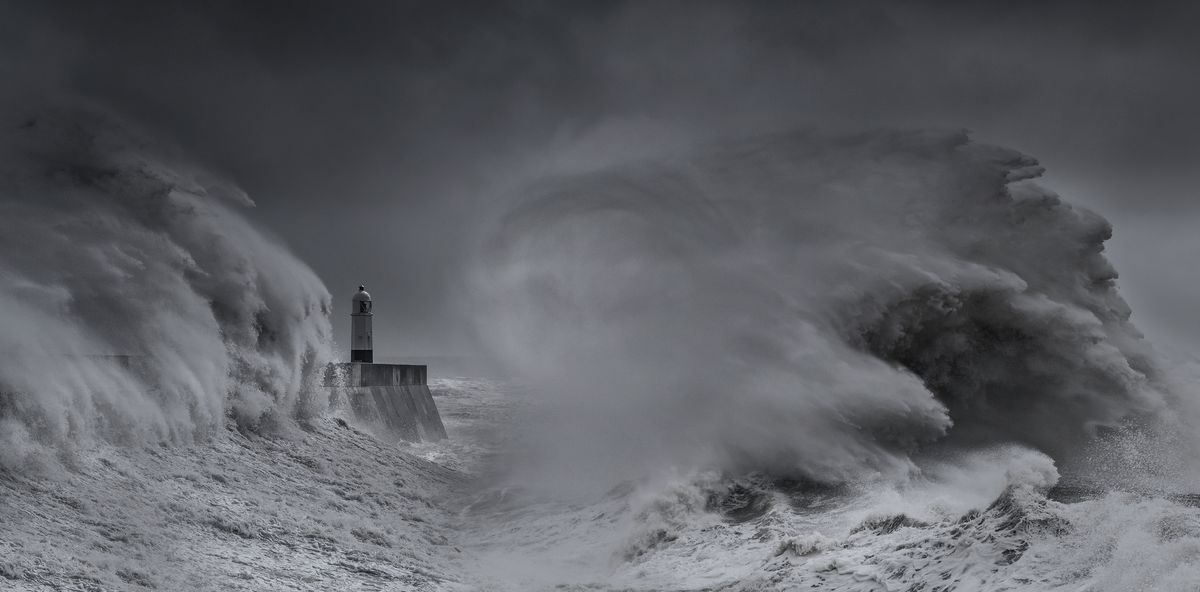 Black-and-white landscape photograph of Porthcawl Lighthouse being battered by crashing waves during a storm 