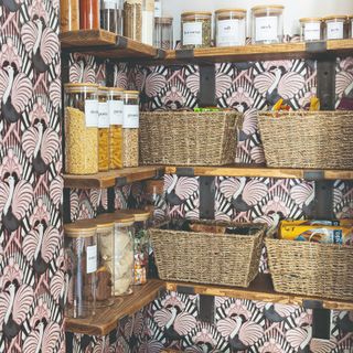 A small pantry with open shelving, storage baskets and unified storage jars with the room covered in a peacock-print wallpaper