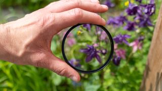 The Kenko PRO1D+ UV filter being held in front of some flowers