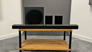 LG S95TR soundbar package from front showing soundbar and speakers on wooden AV rack