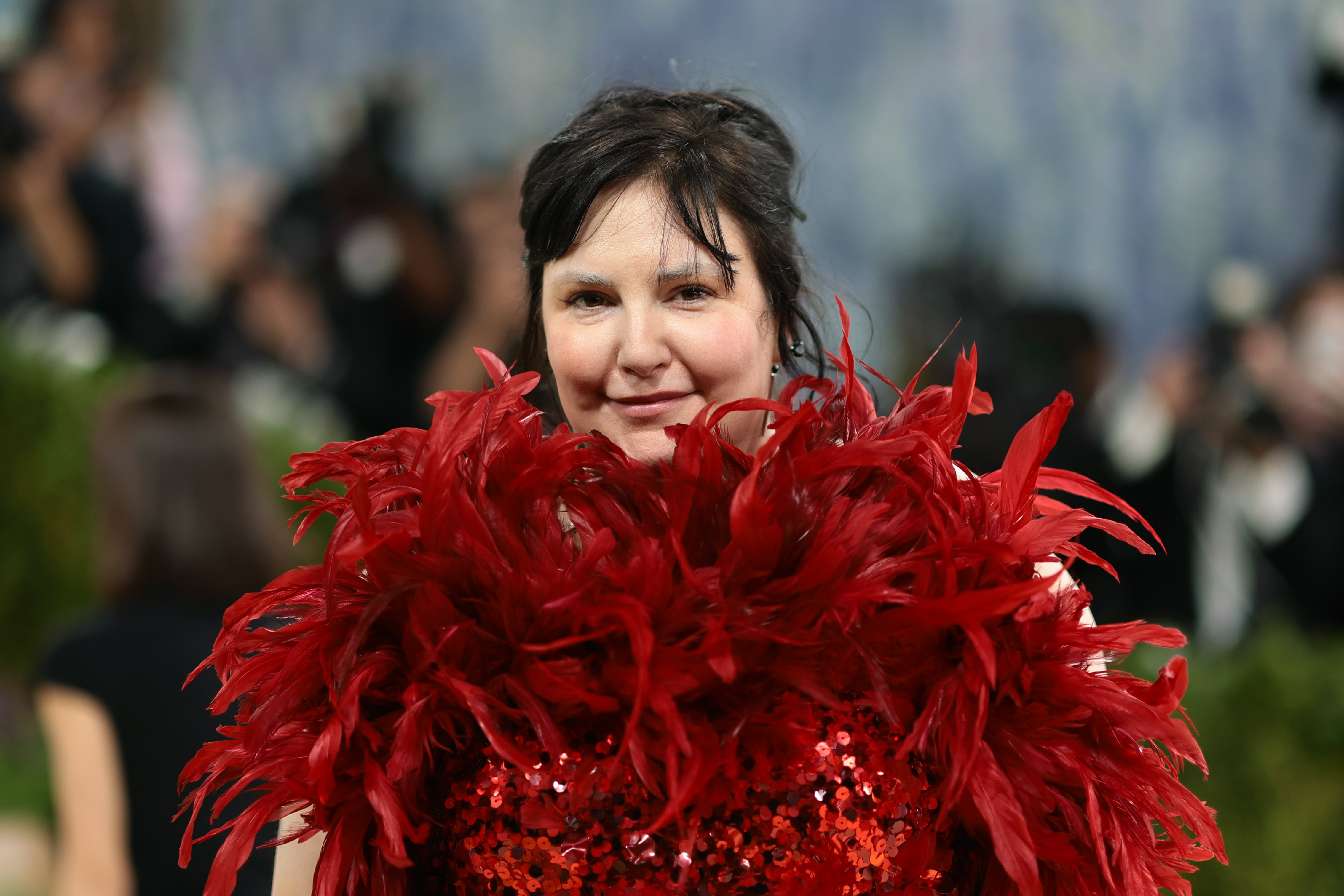a pale woman with brunette bangs in a red feather dress