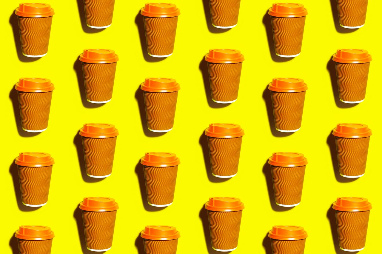 Coffee cup with orange lid on a yellow desk.