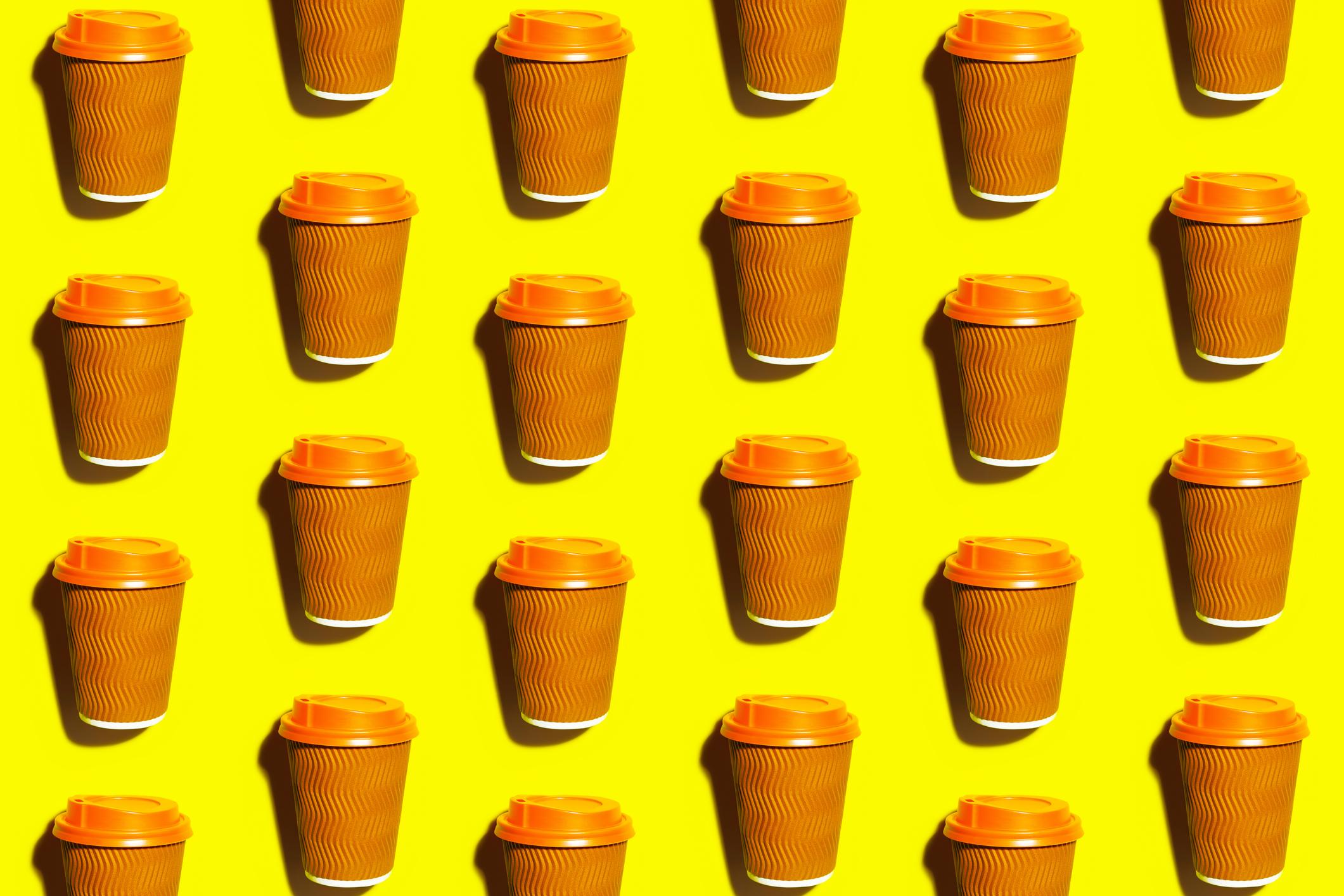 Coffee cup with orange lid on a yellow desk. 
