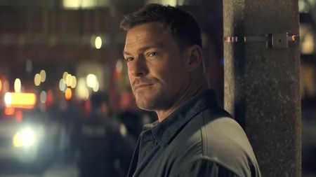 Reacher leaning against street post while slightly grinning in Neagley Season 1