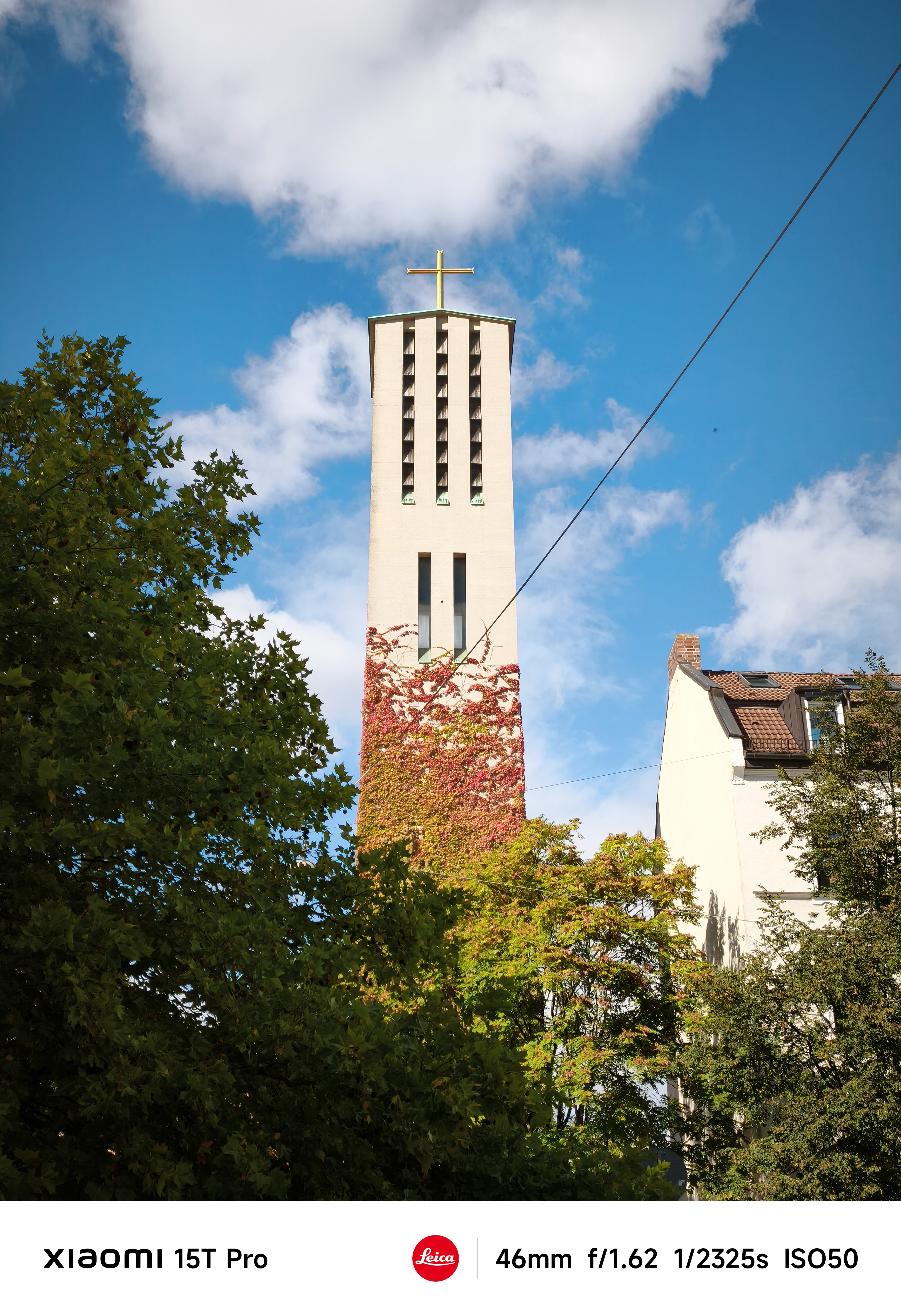A tall church by covered in ivy surrounded by green trees