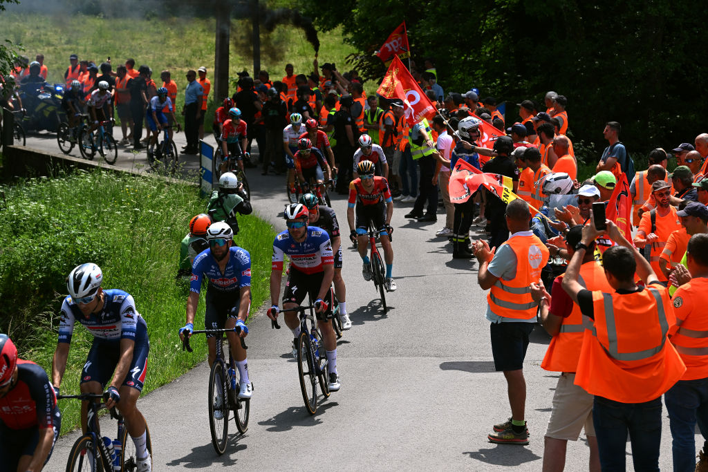 Riders heading past a protest on stage 3 of the 2023 Critérium du Dauphiné