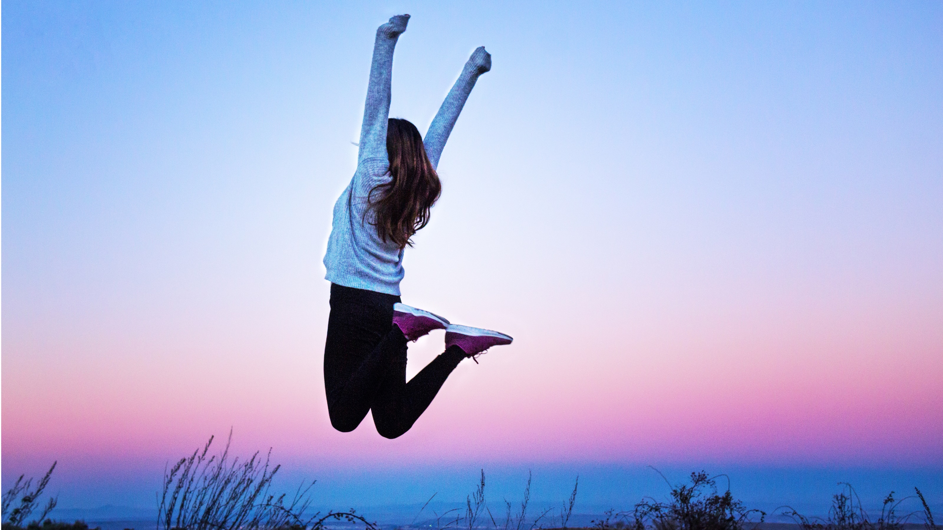 A woman jumps with her arms above her head in celebration.
