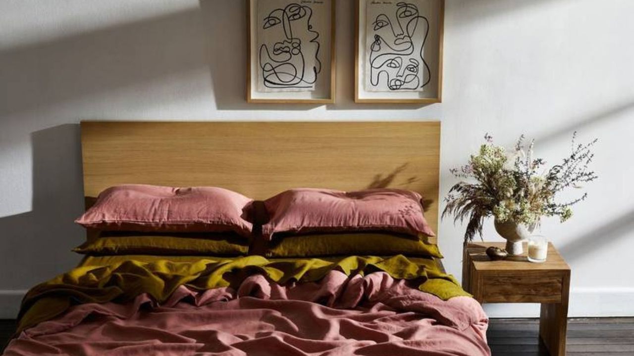 Pink, brown, and green bedding on a wood bed frame against a white wall. 