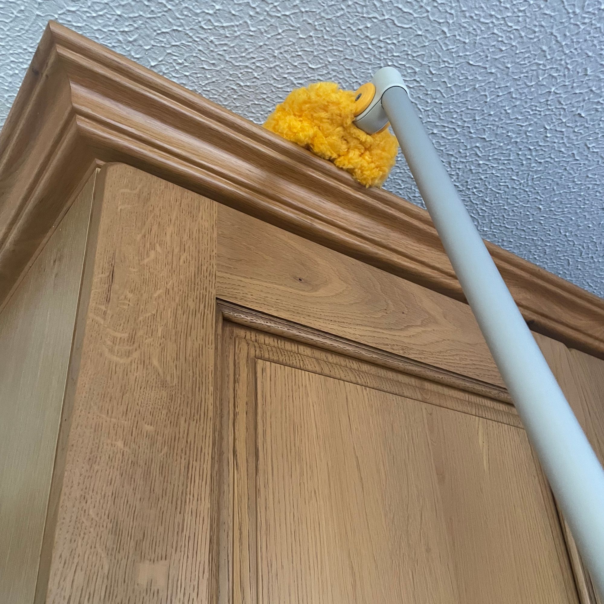 Using the Joseph Joseph Cleantech Adjustable Microfibre High Reach Duster to clean the top of wooden kitchen cabinets