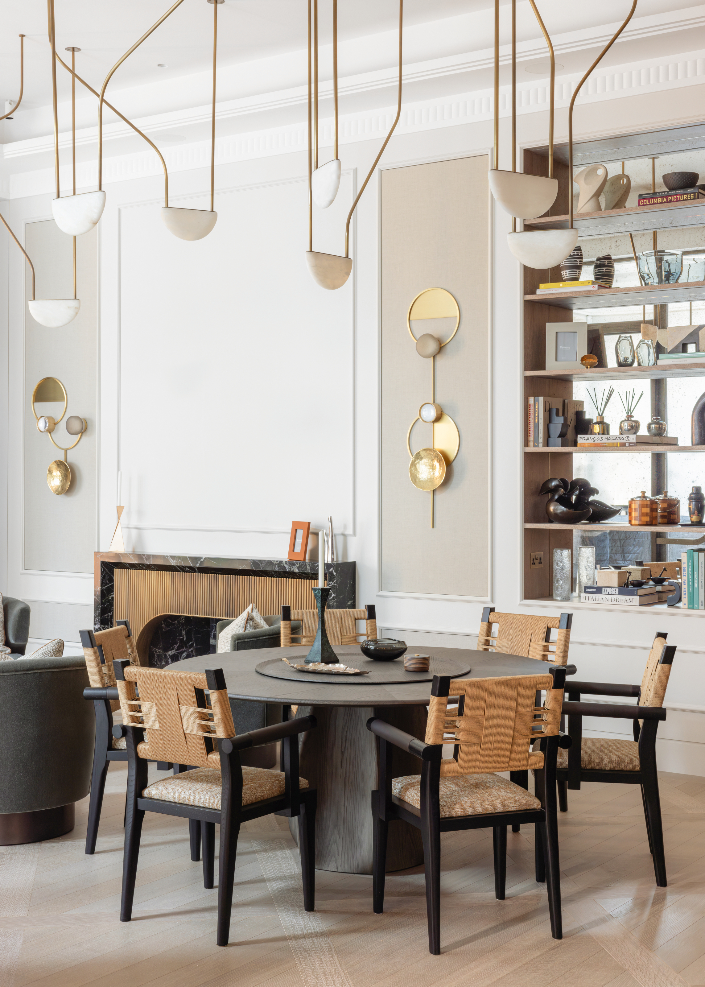 Games area with grey round table, black and rattan chairs, and gold wall lights against beige panelled wall