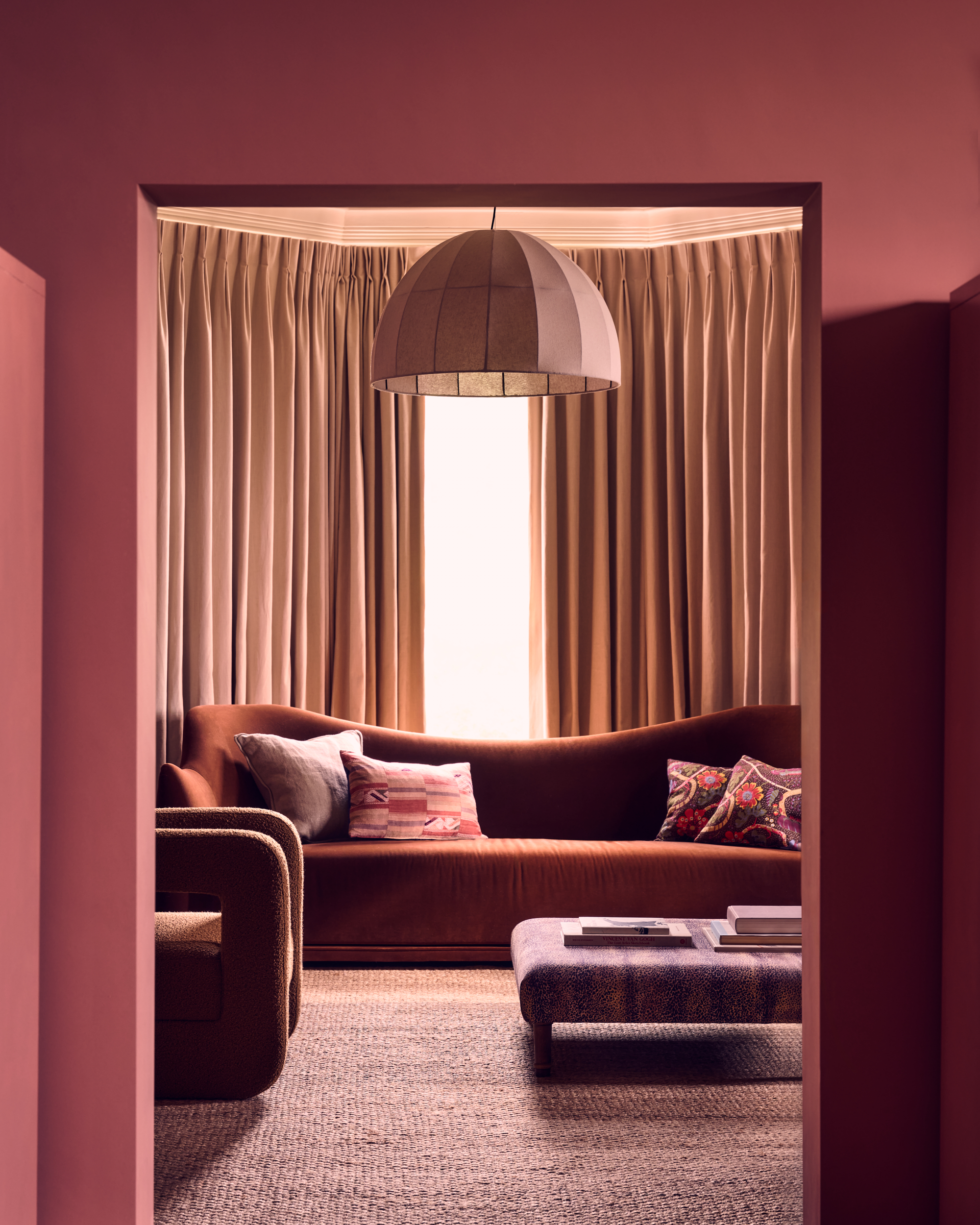 Chalky red living room with brown velvet curved sofa, dome pendant light and beige curtains