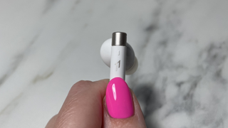 Photo of a hand holding one of the PistonBuds Pro Q30 earbuds by its post, showing the small touch control area.
