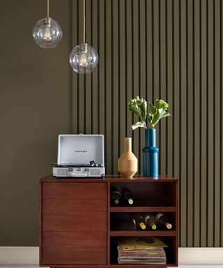 A dresser with a record player and vase in front of an olive green wall