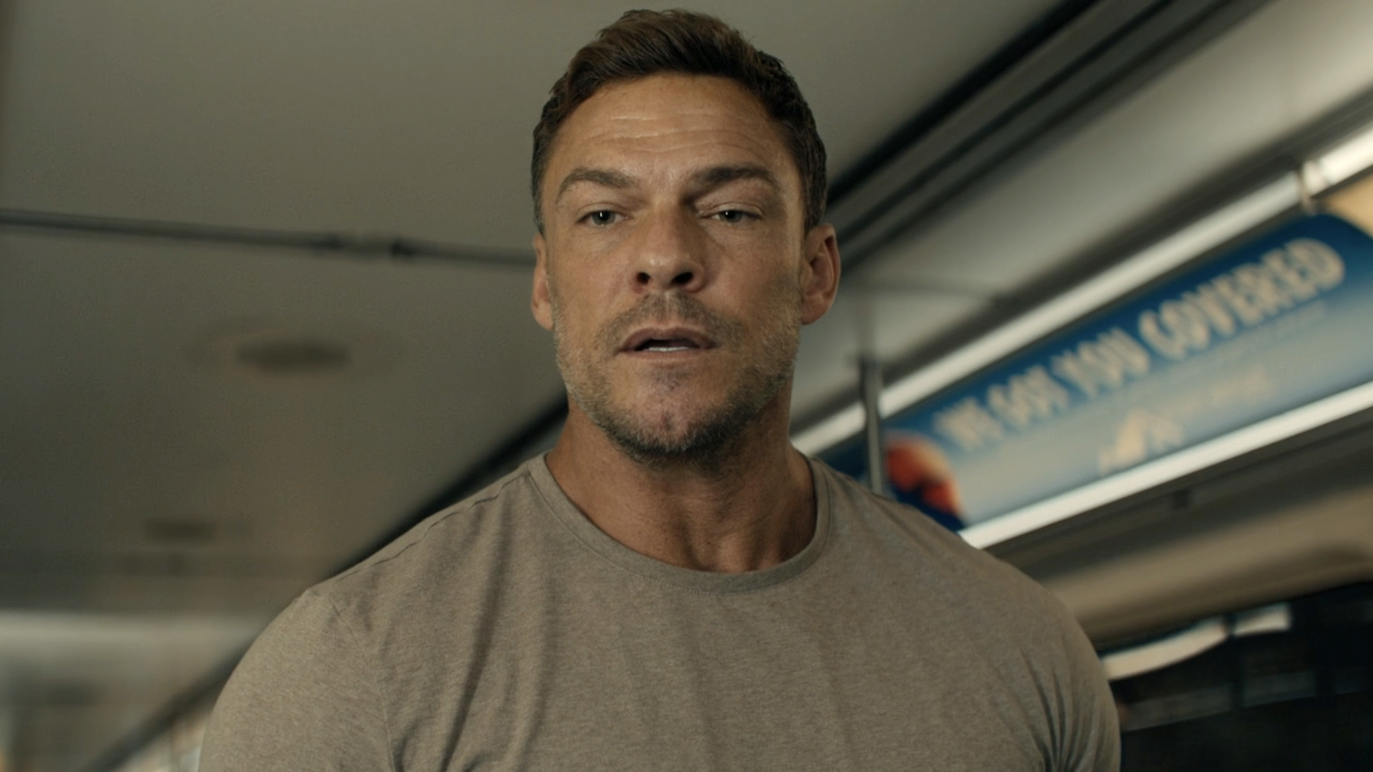 Alan Ritchson as Jack Reacher, wearing a grey t-shirt on a subway train, in season 4 of Reacher.