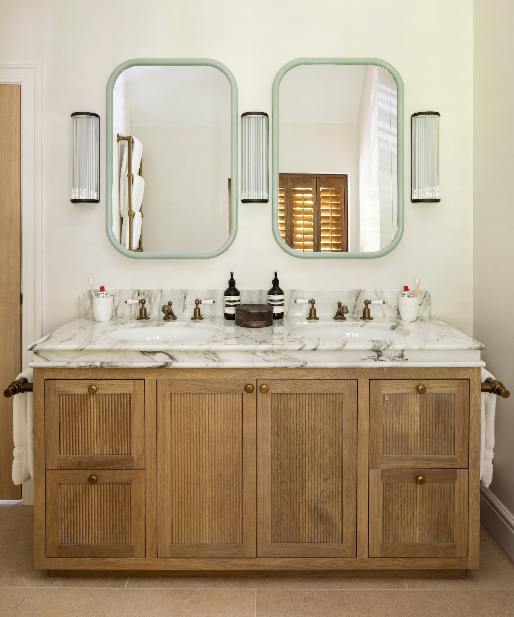 a neutral primary bathroom with an oak reeded vanity and a statement profiled marble top with two mint green mirrors