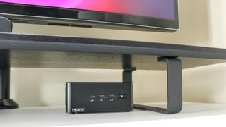 The Asus NUC 14 Pro under a monitor shelf on a desk