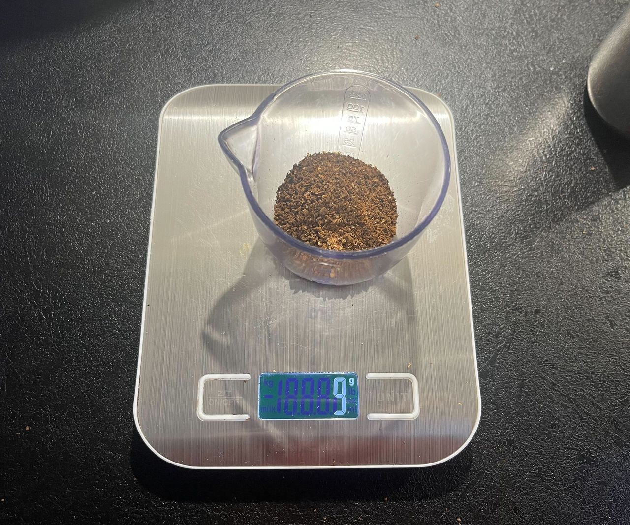 Course ground coffee beans in a clear plastic container on digital weight scales.