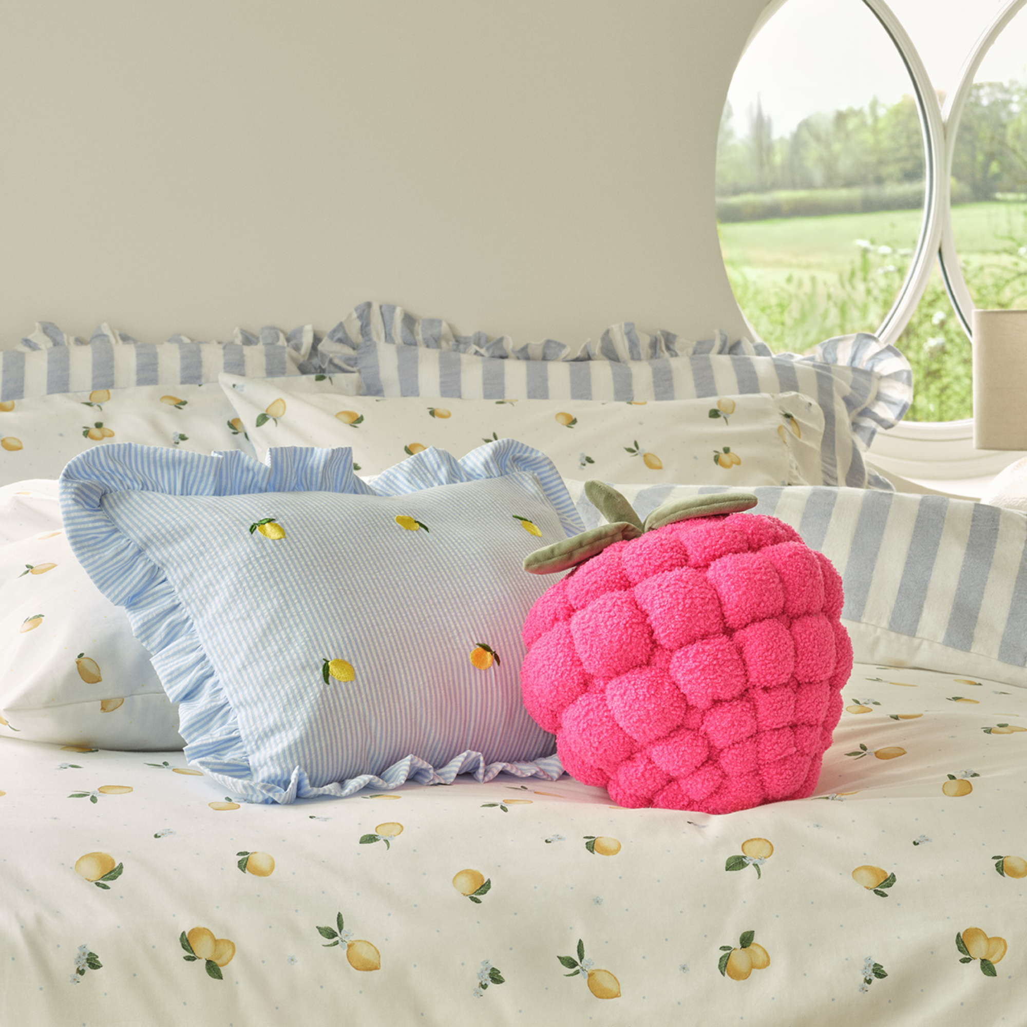 Pink 3D raspeberry shaped cushion on a double bed with lemon printed bedding.