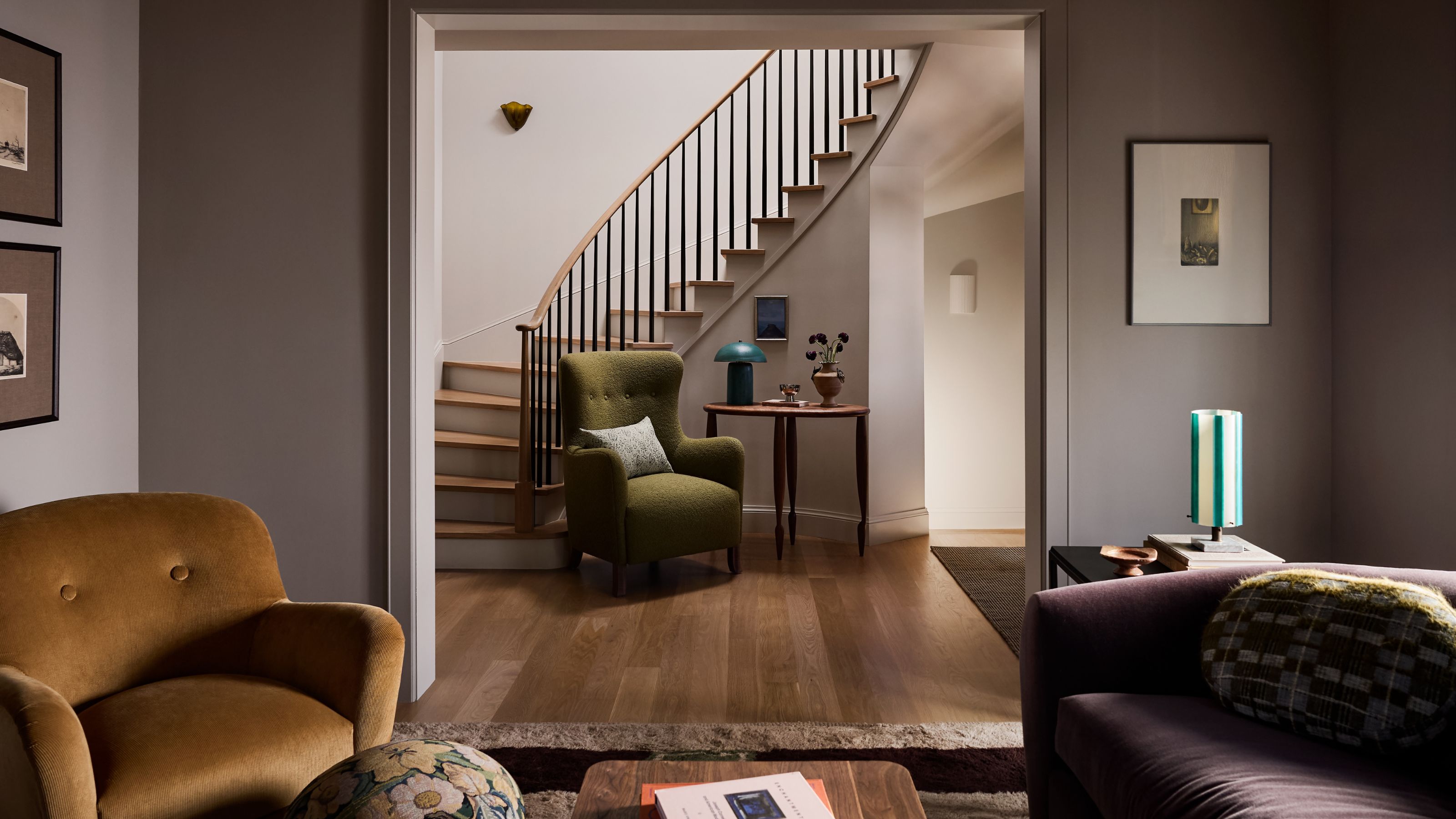 a cozy living room looking through an opening to the entry hall with a curved staircase
