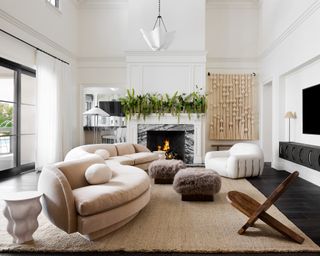 Living room with curved sofa in neutral fabric, armchair and chair on neutral rug in room with white walls