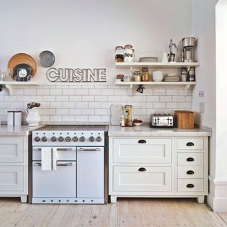 A white kitchen with white metro tiles above an oven and below a cuisine sign