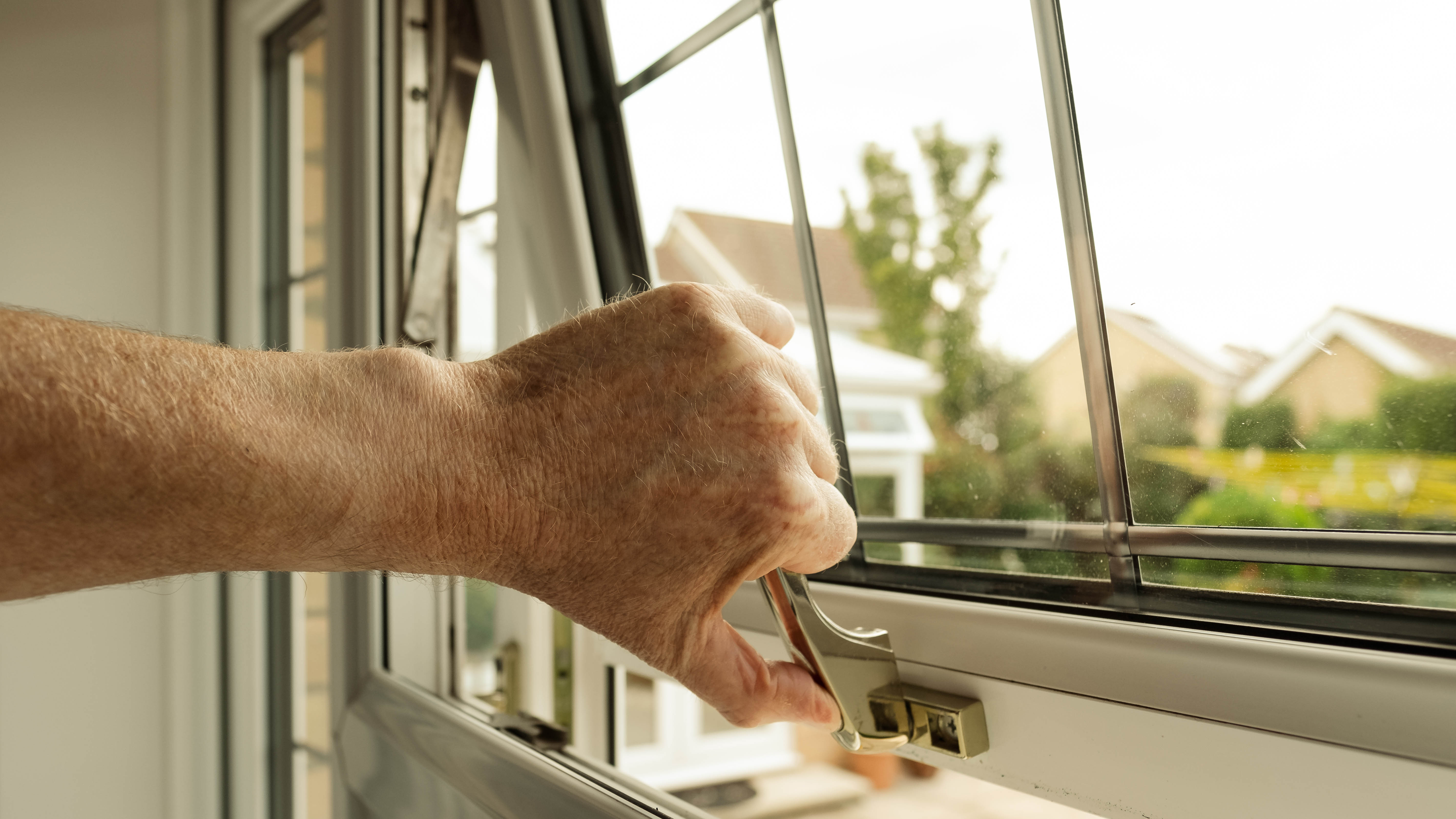 An open window being closed by hand