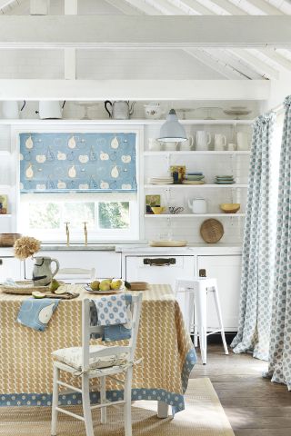 White kitchen with blue and yellow accessories and upholstery and open wooden shelving.