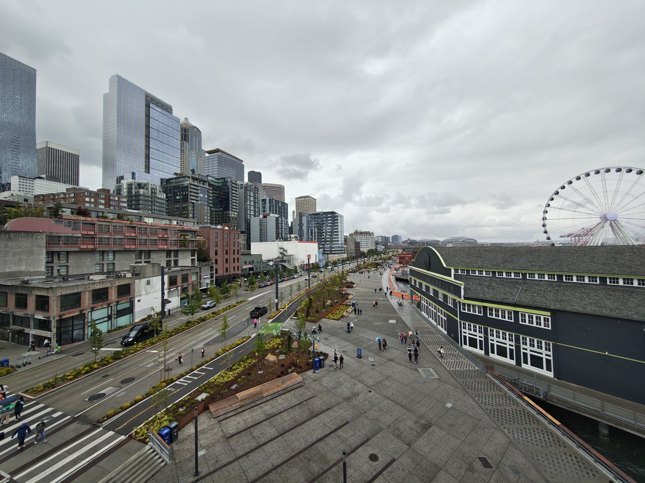 The Seattle waterfront with people walking around, a Ferris wheel on the right, and the city on the left