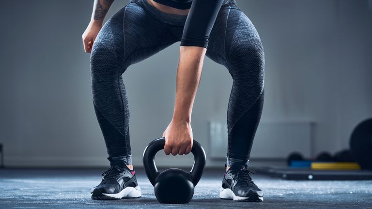 Person is in a mid squat position as they go to lift a kettlebell from the ground