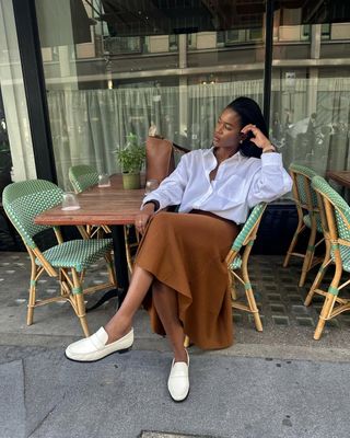 @nlmarilyn wearing cream loafers with a tan midi skirt and a white button up shirt