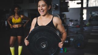 Smiling woman carrying weight plate in gym