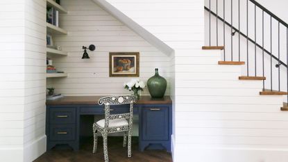 Home office built under stairs with blue desk and shiplap walls