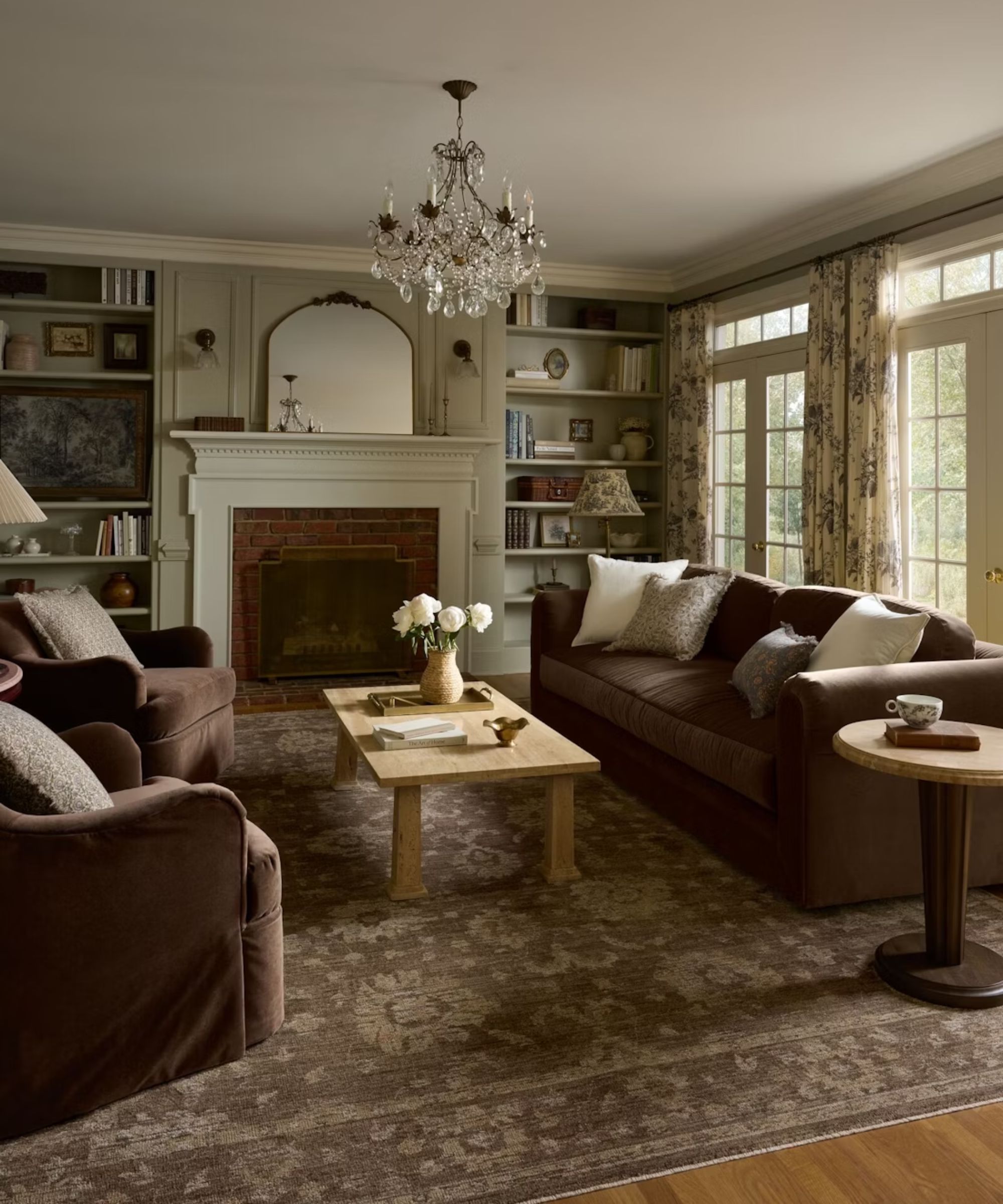 cozy warm living room with a traditional fireplace, shelving, a brown vintage rug and brown velvet couch and two swivel chairs