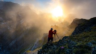 Photographer with tripod on rocks looking at the sky at sunset above lake Limmernsee, Canton of Glarus, Switzerland