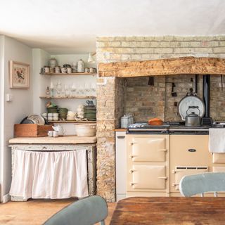 Rustic cottage kitchen with cream aga in brick fireplace recess, vintage kitchenalia and vintage cupboard with fabric skirt